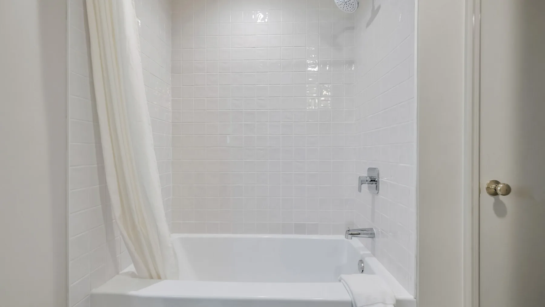 A bathroom shower and tub with a curtain and tiled walls.