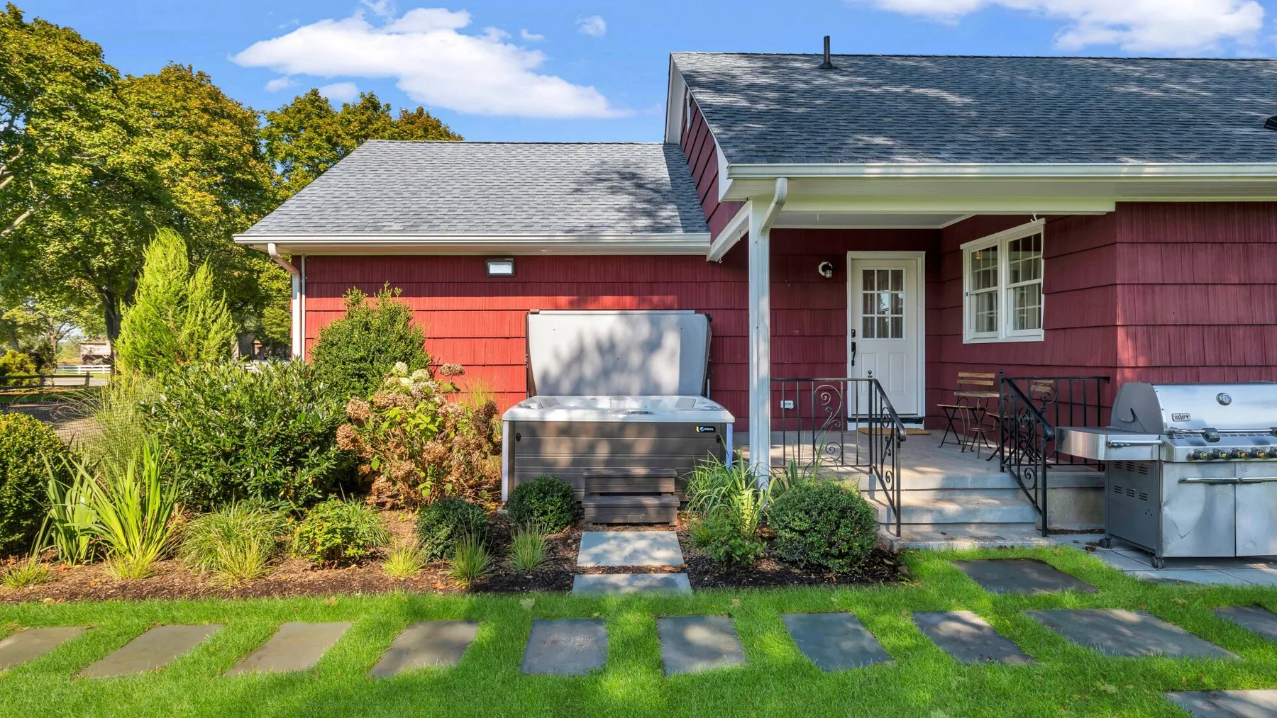 A red house with an outdoor patio, grill, and stepping stones across the lawn.