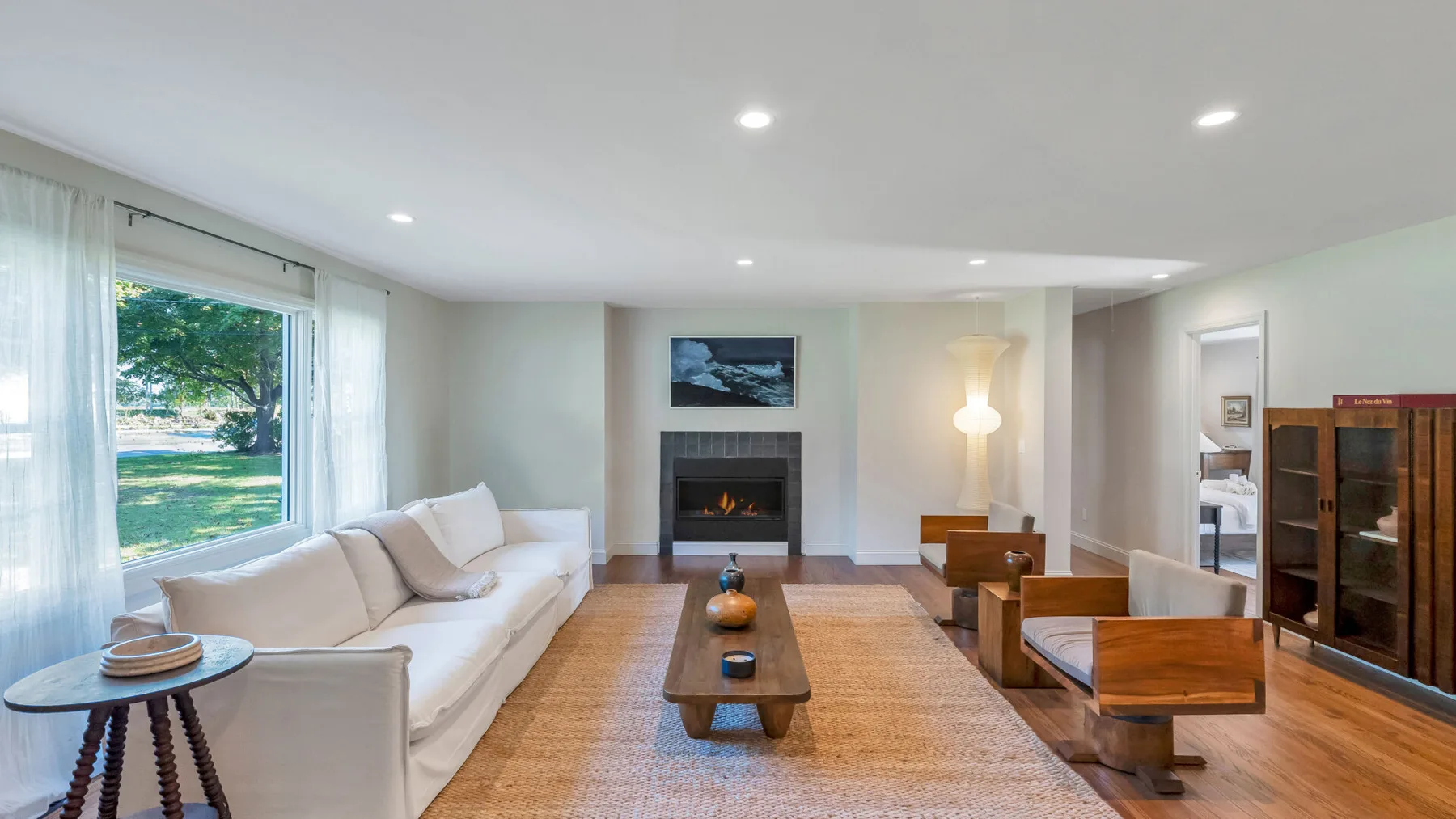 A bright living room has white seating, a coffee table, and a fireplace.