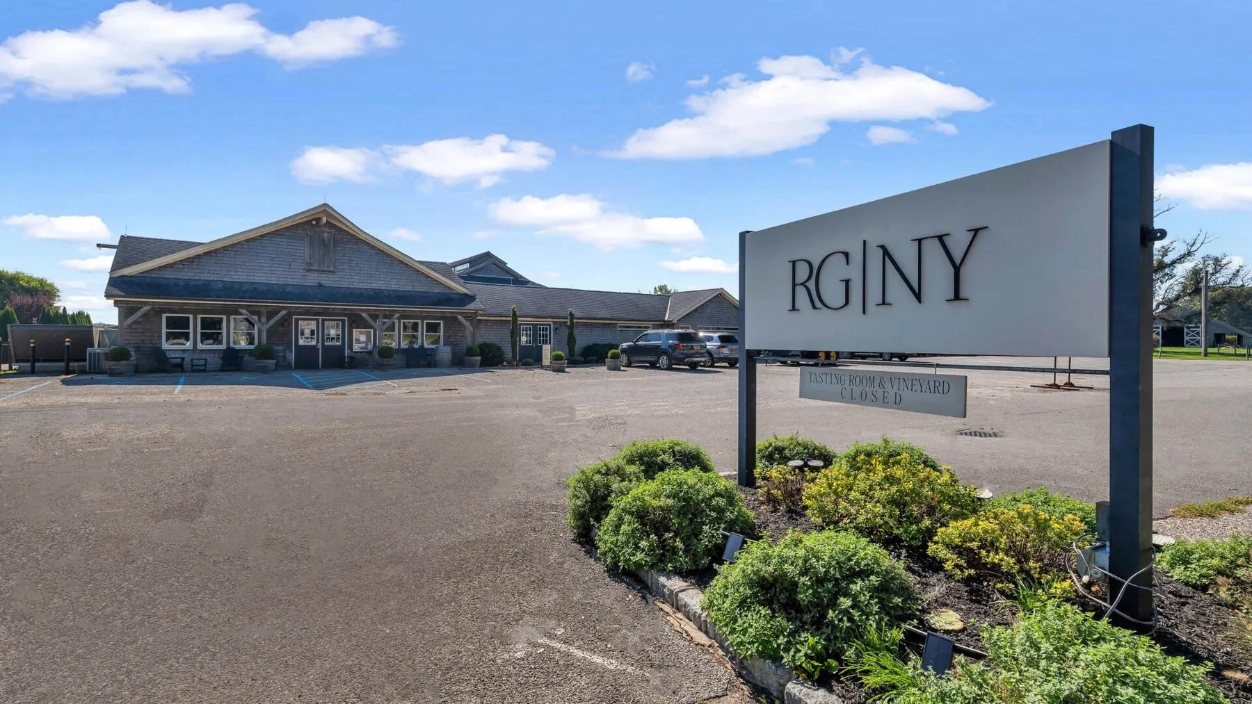 A roadside sign stands beside landscaped shrubs in front of a low commercial building.