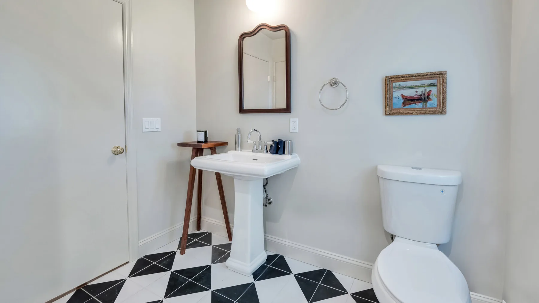 A bathroom with a pedestal sink, toilet, and black-and-white tiled floor.