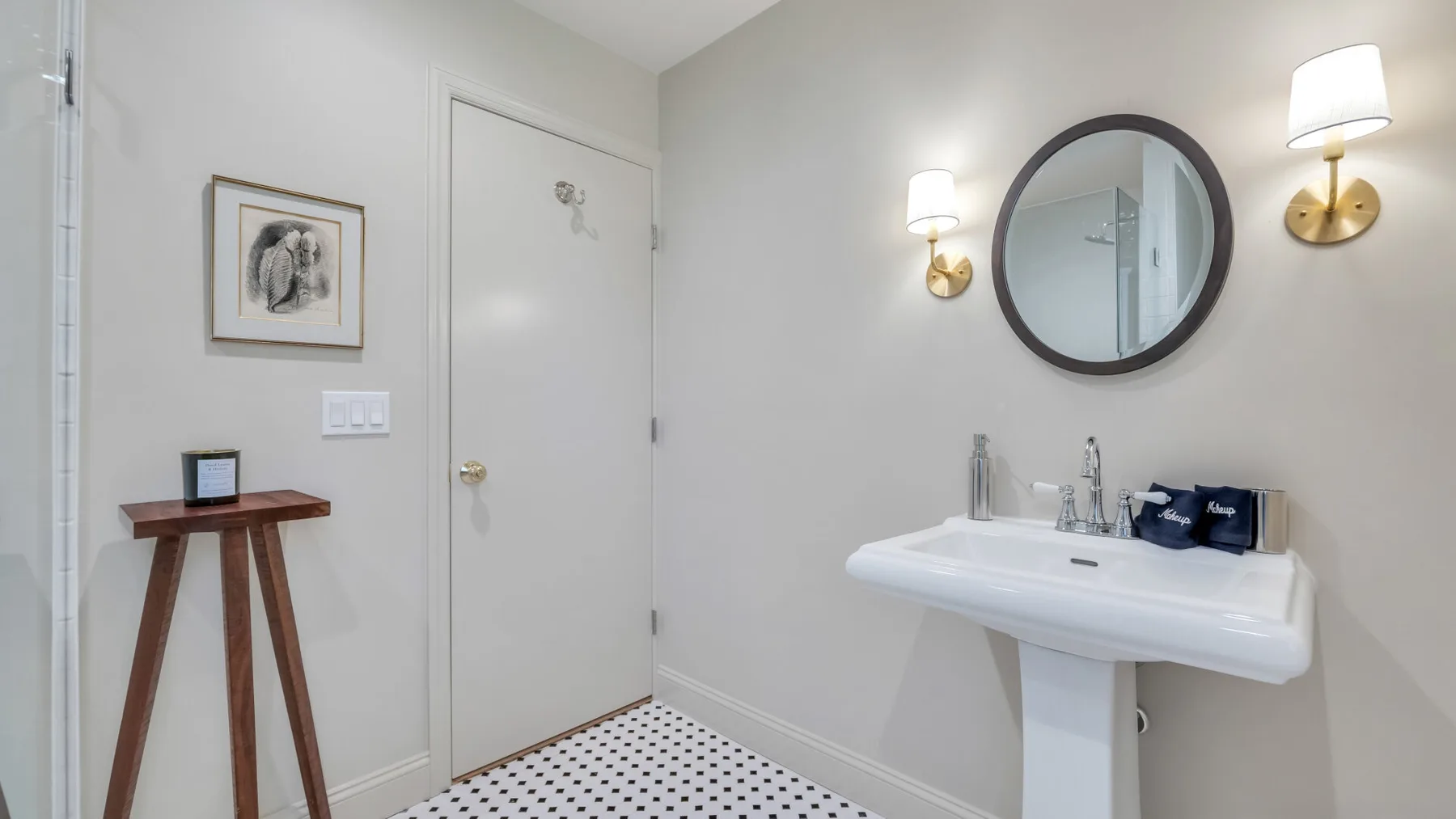 A bright bathroom with a pedestal sink and round wall mirror.