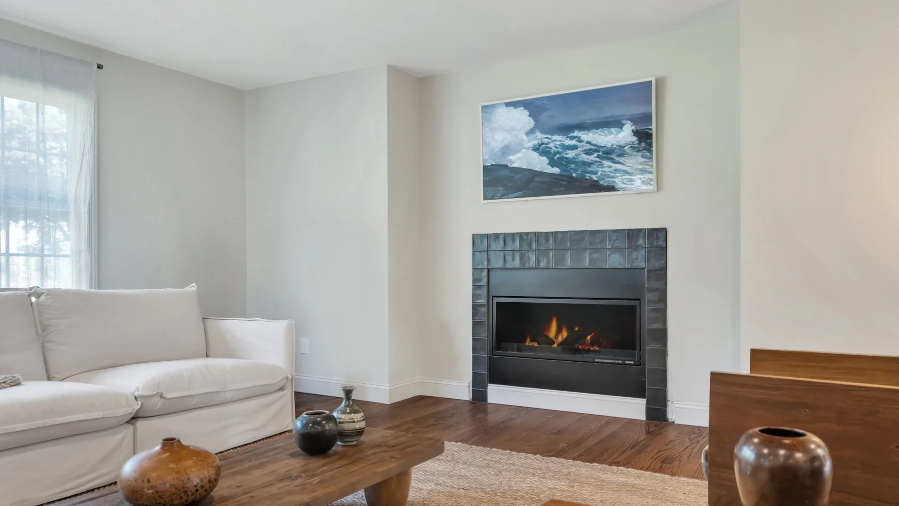 A living room with seating, a fireplace, and a seascape picture on the wall.