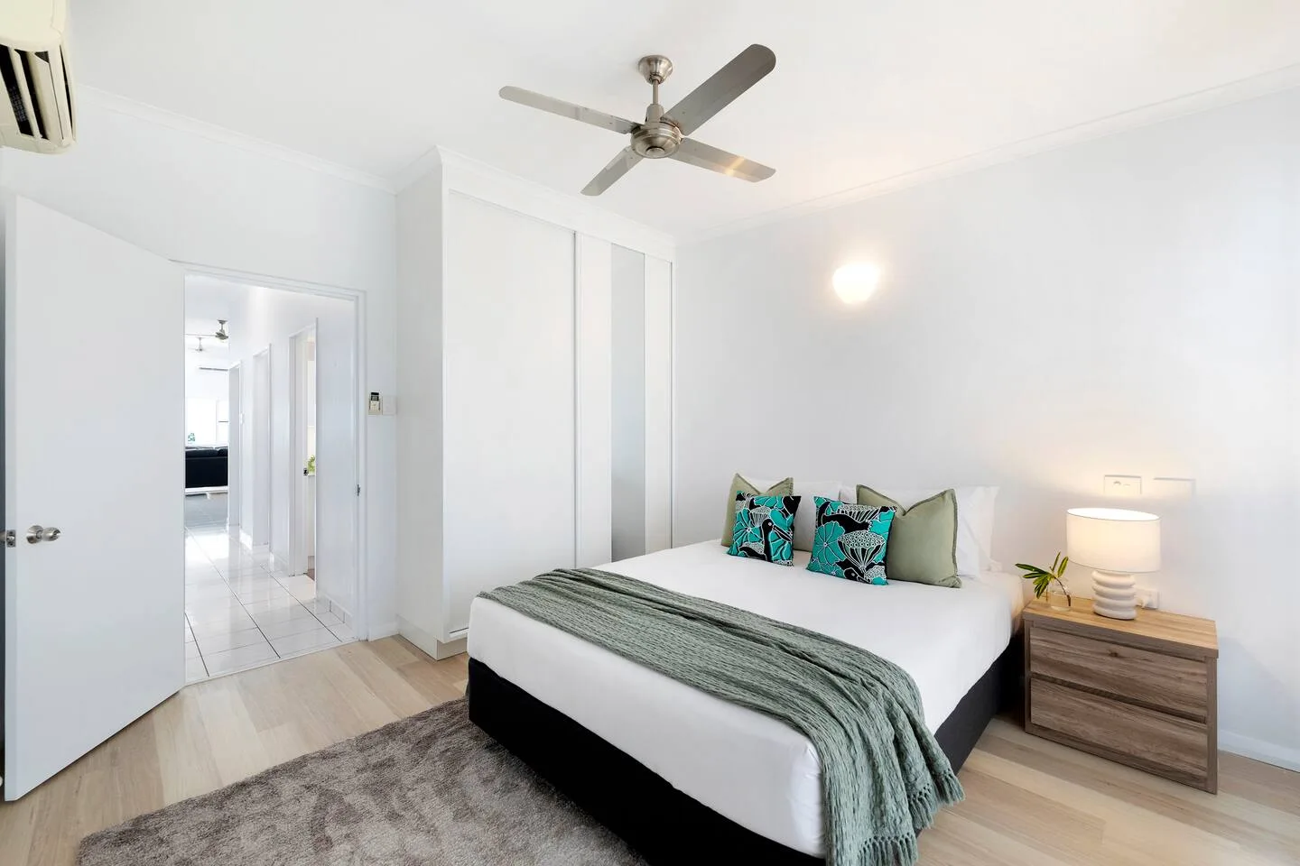 Un dormitorio con una cama, almohadas estampadas y una mesa de noche.