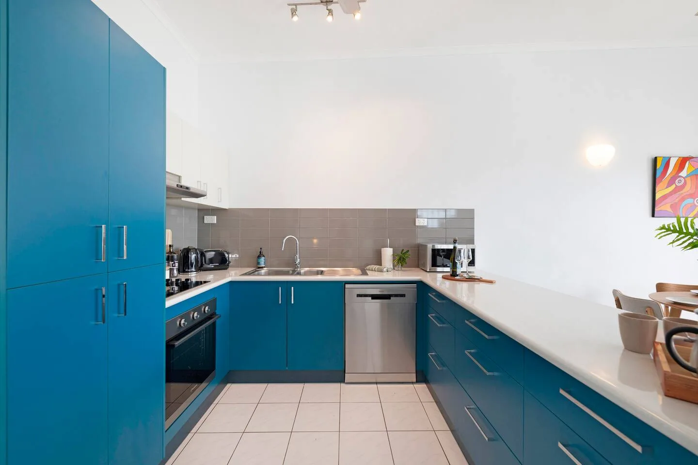 Una cocina luminosa con gabinetes azules, un salpicadero de azulejos y una encimera larga.