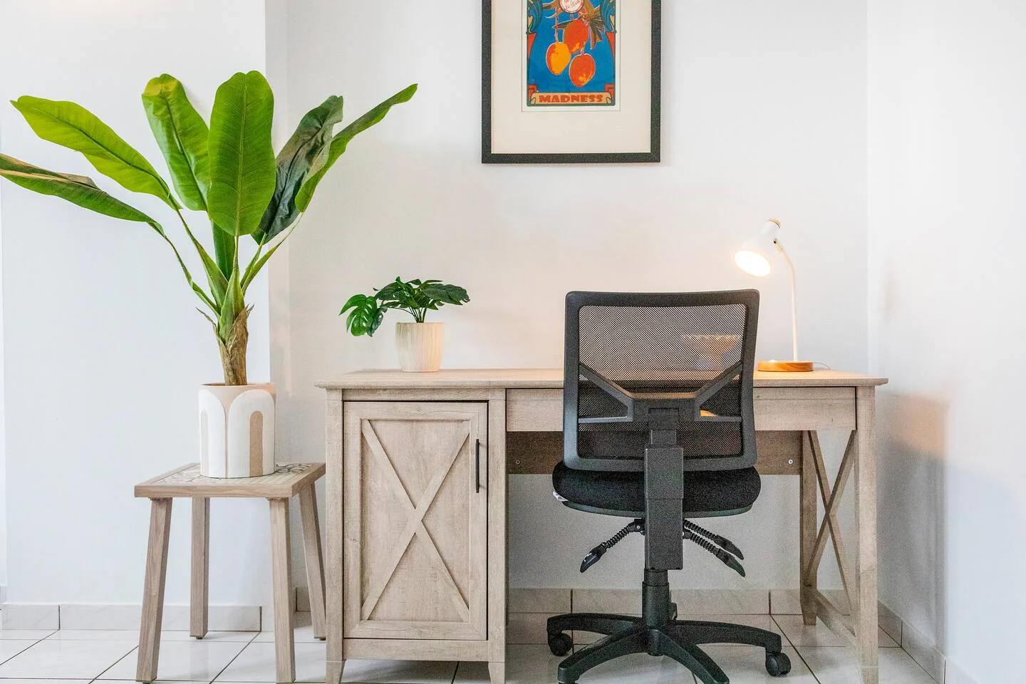 Un escritorio y una silla de oficina están junto a una pared blanca y dos plantas.