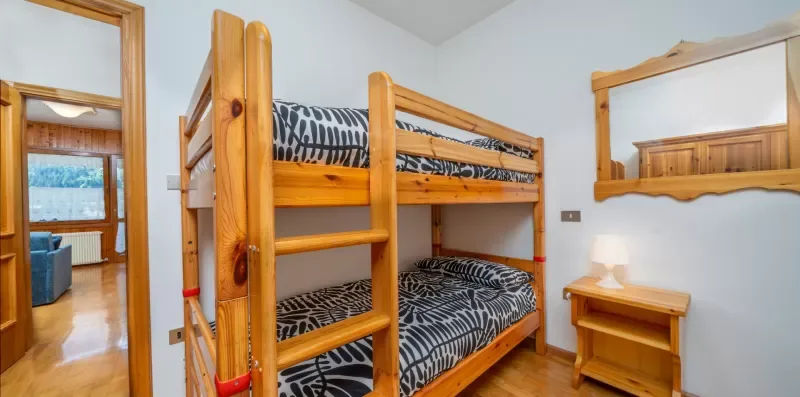 A bedroom with a wooden bunk bed and patterned bedding.