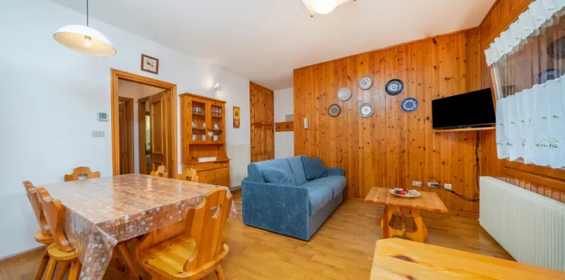A wood-paneled living and dining room with a blue sofa and a table.