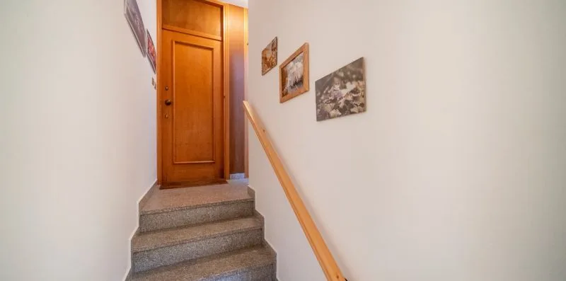 A narrow staircase leads up to a wooden door, with a handrail and wall pictures.