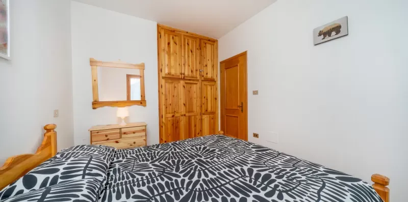 A bedroom with patterned bedding, wooden wardrobes, and a mirror above a dresser.