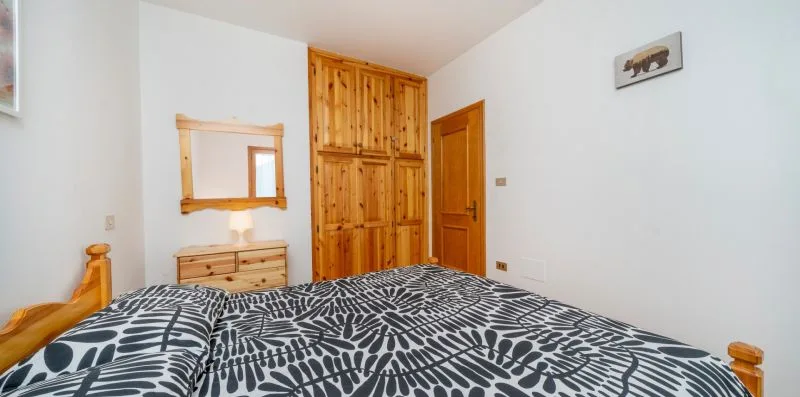 A bedroom with a patterned bedspread, wooden wardrobe, and mirror.