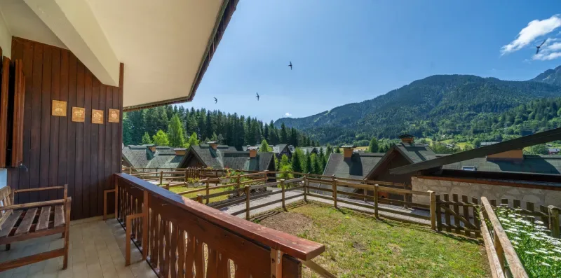 A balcony overlooks fenced grounds and rooftops, with forested mountains in the distance.