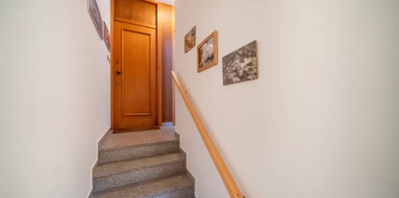 A short interior staircase leads to a wooden door, with framed pictures along the wall.