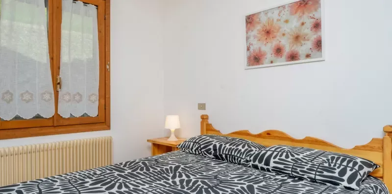 A bedroom with a bed beneath floral wall art and a curtained window.