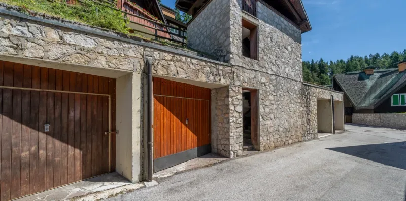 A stone building with wooden garage doors beside a paved driveway.