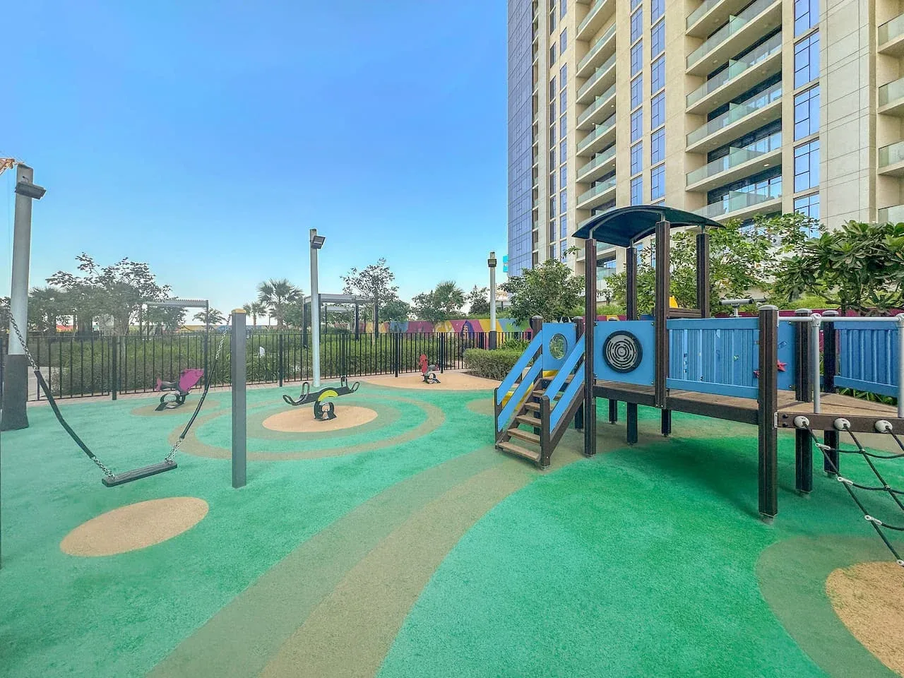 Parque infantil al aire libre con juegos coloridos junto a un edificio residencial alto.