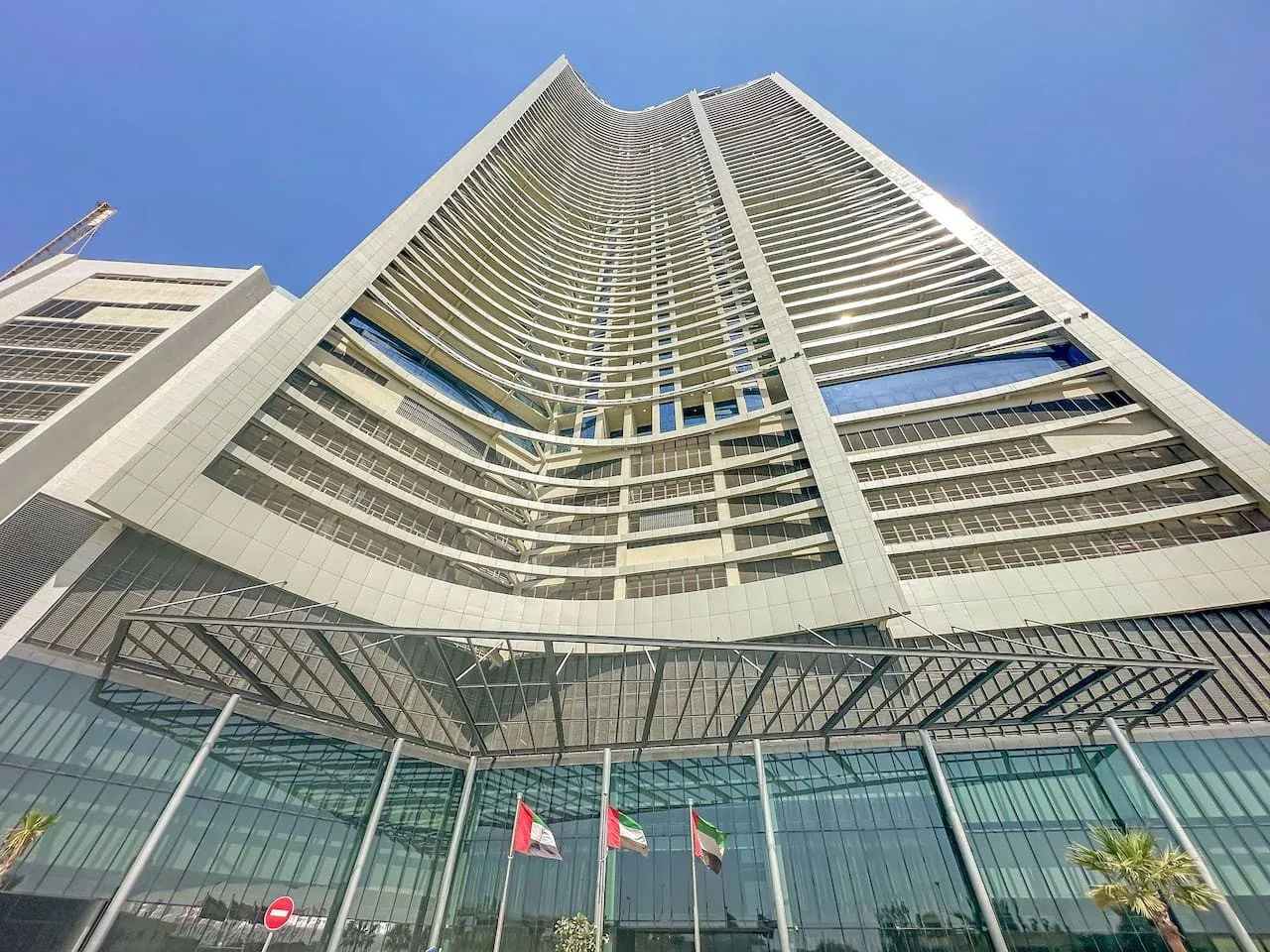 Un edificio alto y curvo se eleva sobre una entrada acristalada bajo un cielo despejado.