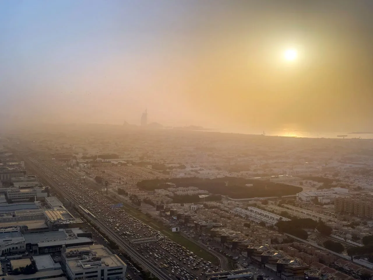 Un paisaje urbano brumoso se extiende hasta el horizonte bajo el sol poniente.