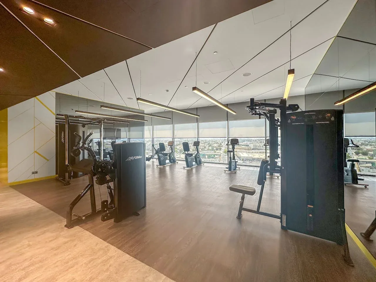 Un gimnasio con máquinas de ejercicio y grandes ventanas con vistas a la ciudad.