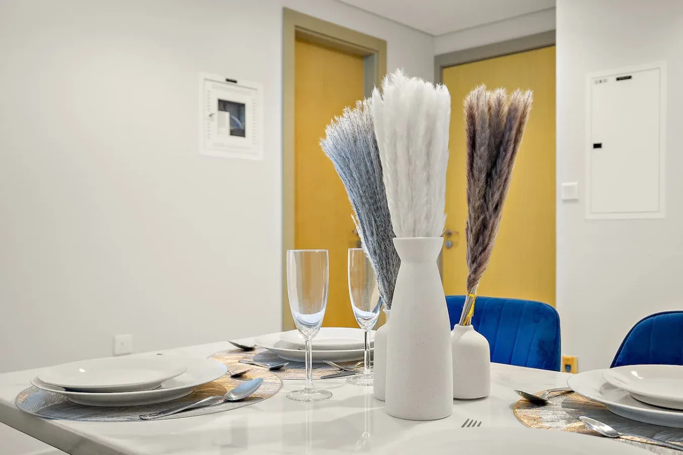 Una mesa de comedor está puesta con platos, copas y jarrones con hierbas secas.