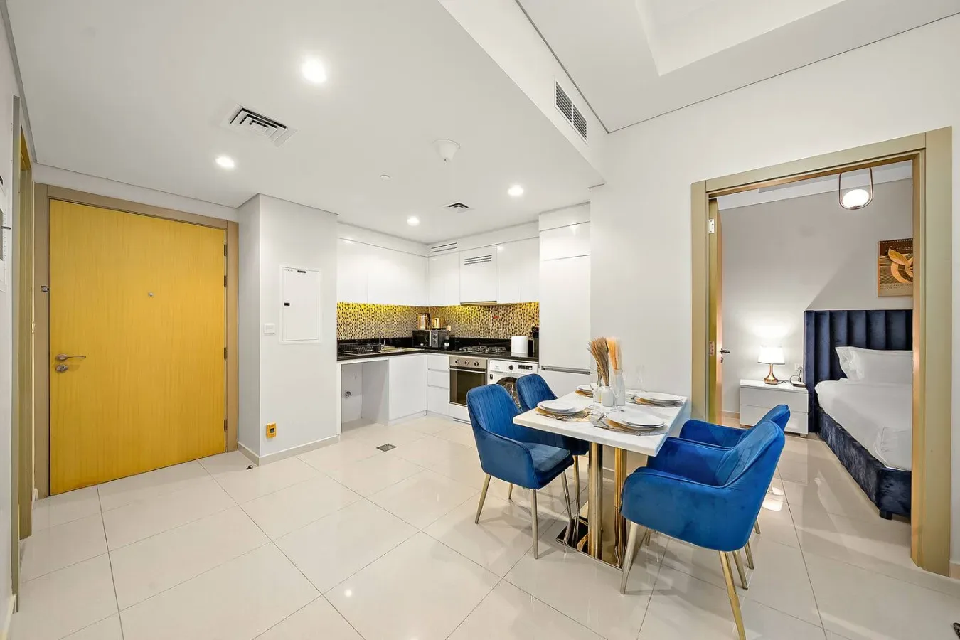 Un comedor luminoso junto a una cocina compacta, con asientos azules alrededor de una mesa.