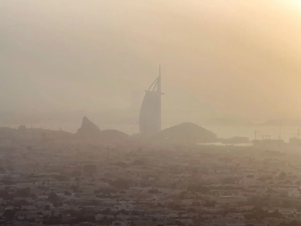 Un horizonte urbano brumoso con una torre en forma de vela cerca de la costa.