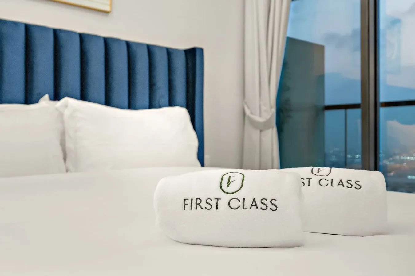 Un dormitorio con ropa de cama blanca, un cabecero azul oscuro y una ventana con cortinas.
