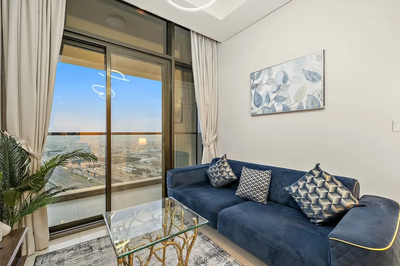 Una sala de estar con un sofá azul junto a una gran ventana con vistas a la ciudad.