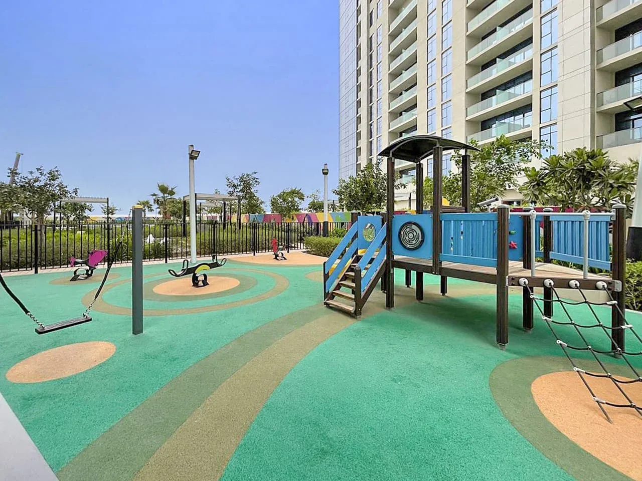 Un parque infantil al aire libre con juegos para trepar y columpios junto a un edificio residencial.