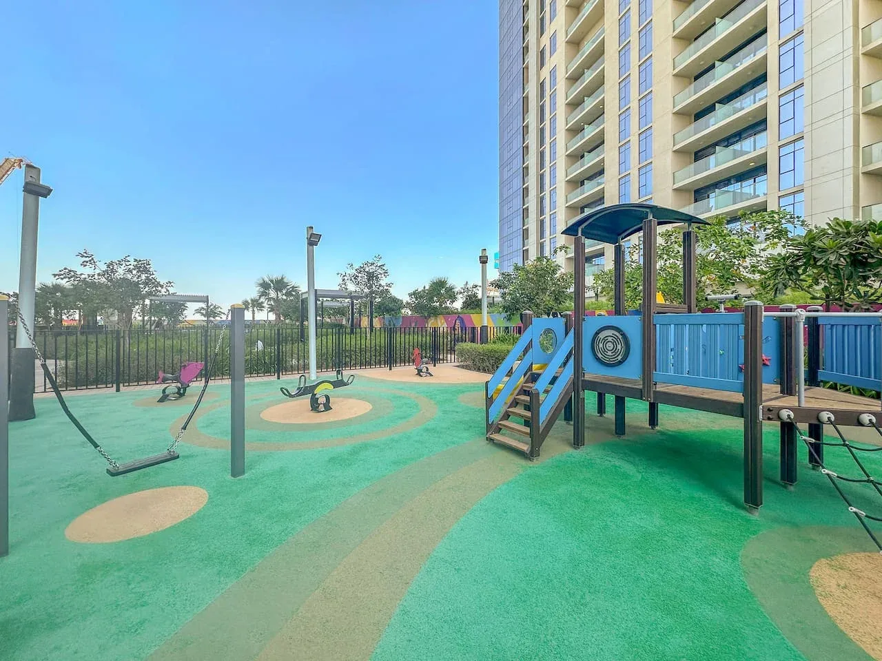 Un parque infantil al aire libre con juegos coloridos junto a un edificio residencial alto.