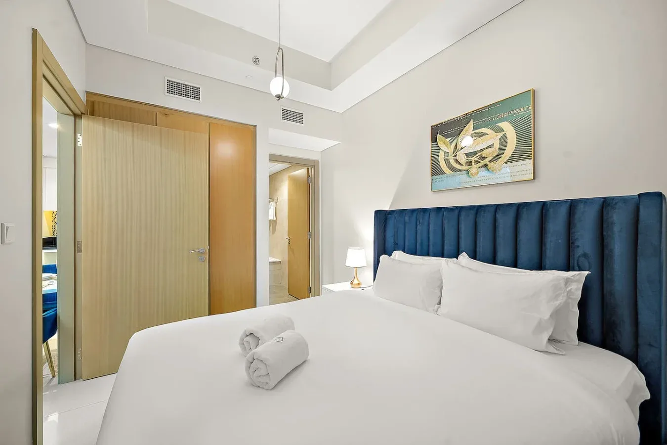 Un dormitorio con una cama blanca, un cabecero azul tapizado y un armario de madera.