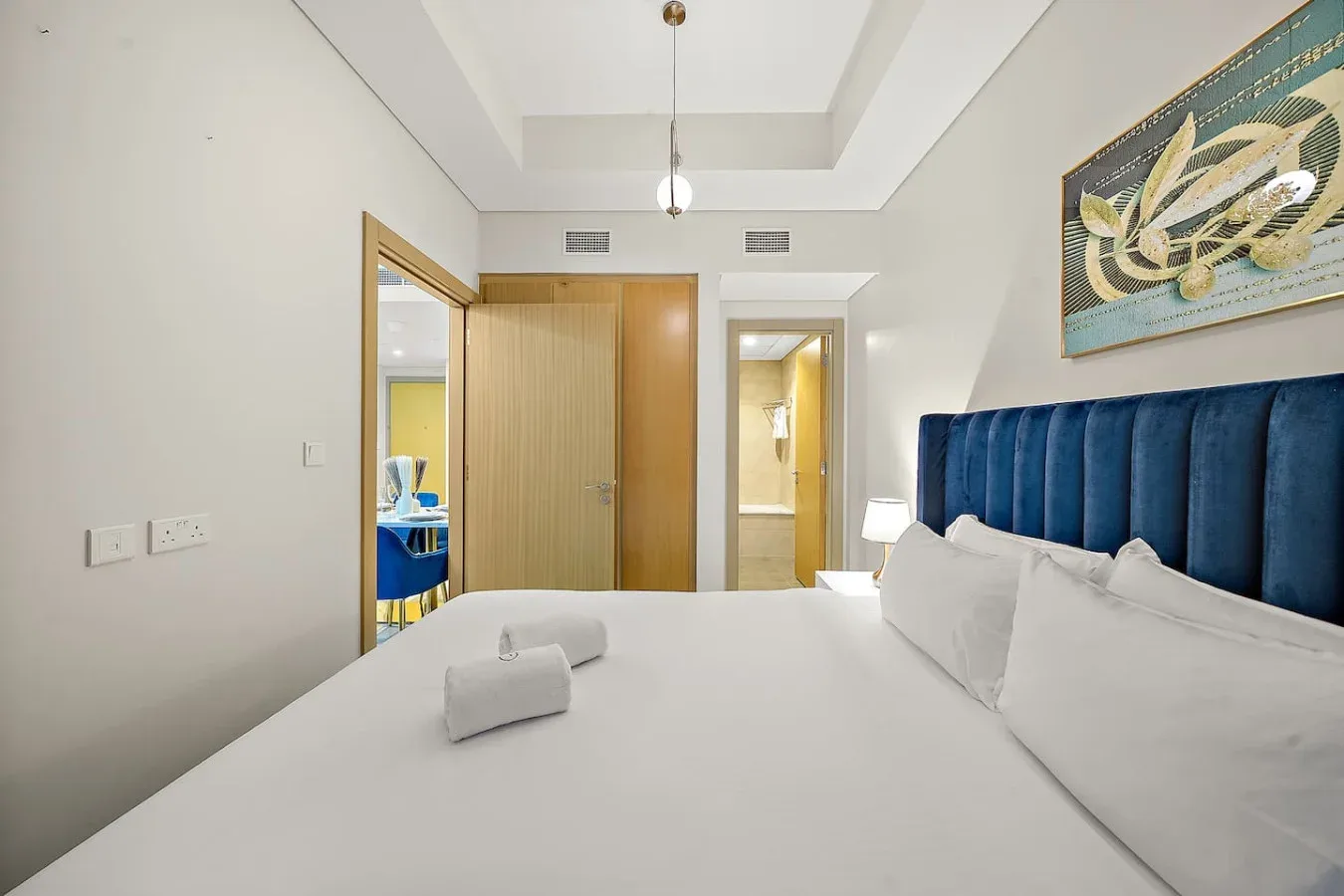 Un dormitorio luminoso con ropa de cama blanca y un cabecero tapizado azul.