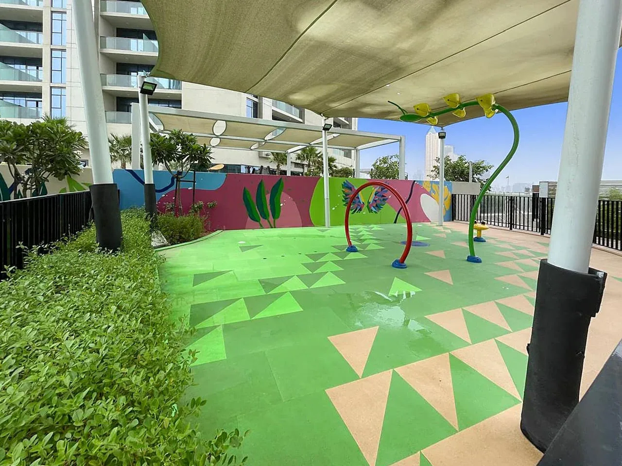 Una zona de juegos al aire libre tiene un suelo verde estampado y una cubierta de sombra.