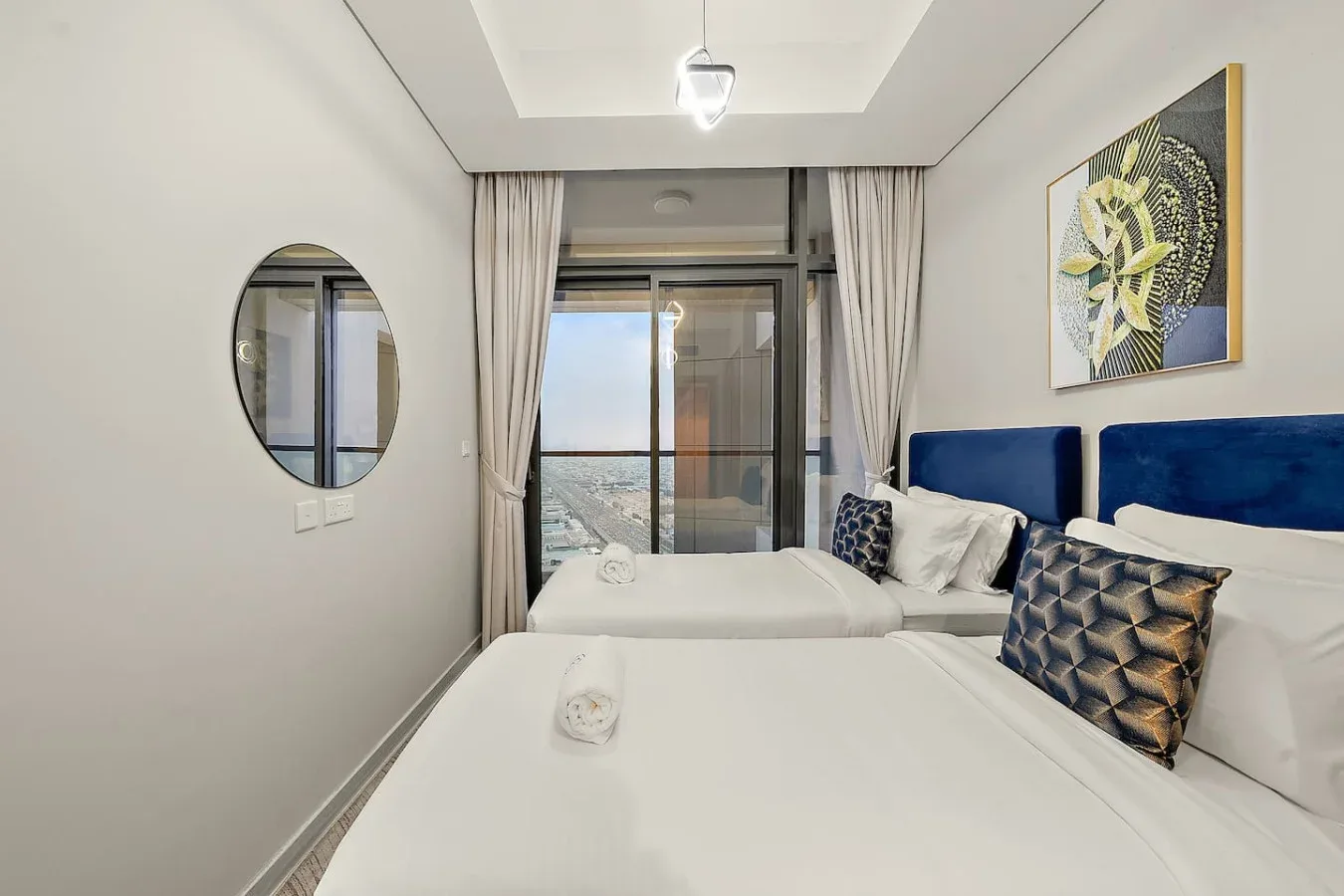 Un dormitorio luminoso con dos camas, cabeceros azules y una ventana grande.