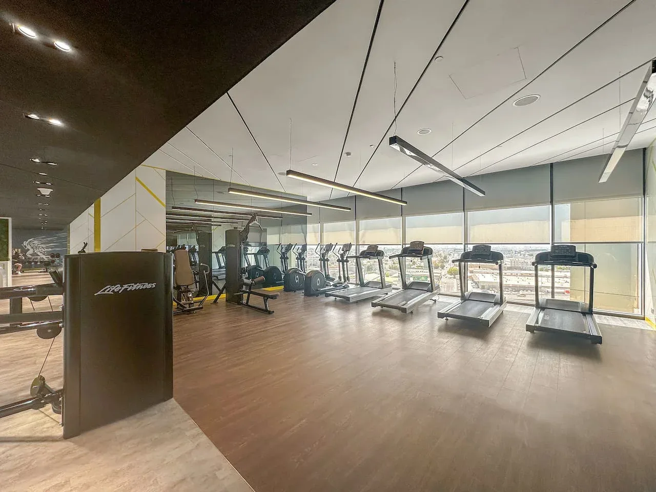 Una sala de ejercicio con cintas de correr y equipos junto a grandes ventanas.