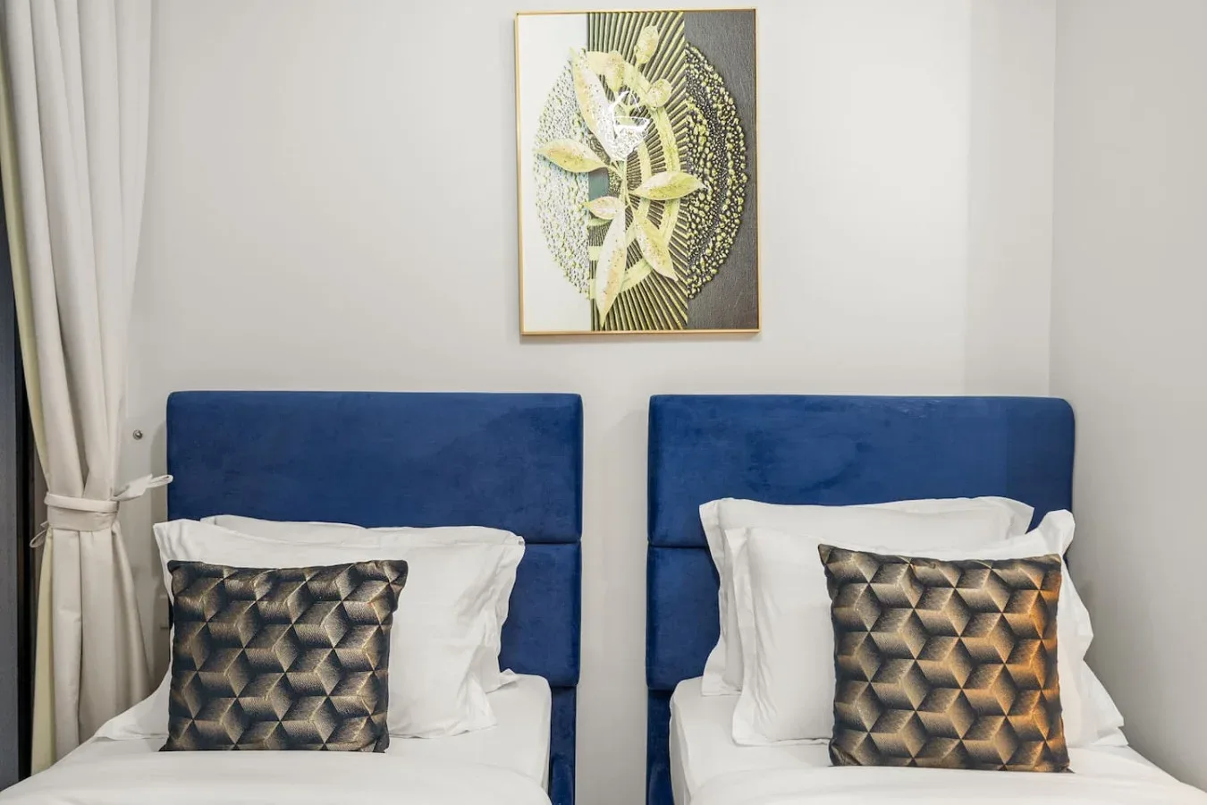 Dormitorio con dos camas, cabeceros azules y un cuadro en la pared.