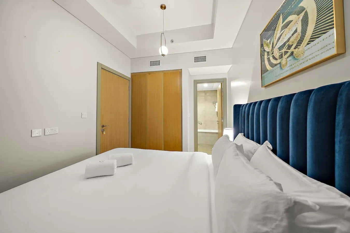 Un dormitorio con una cama blanca, un cabecero azul tapizado y puertas de madera.