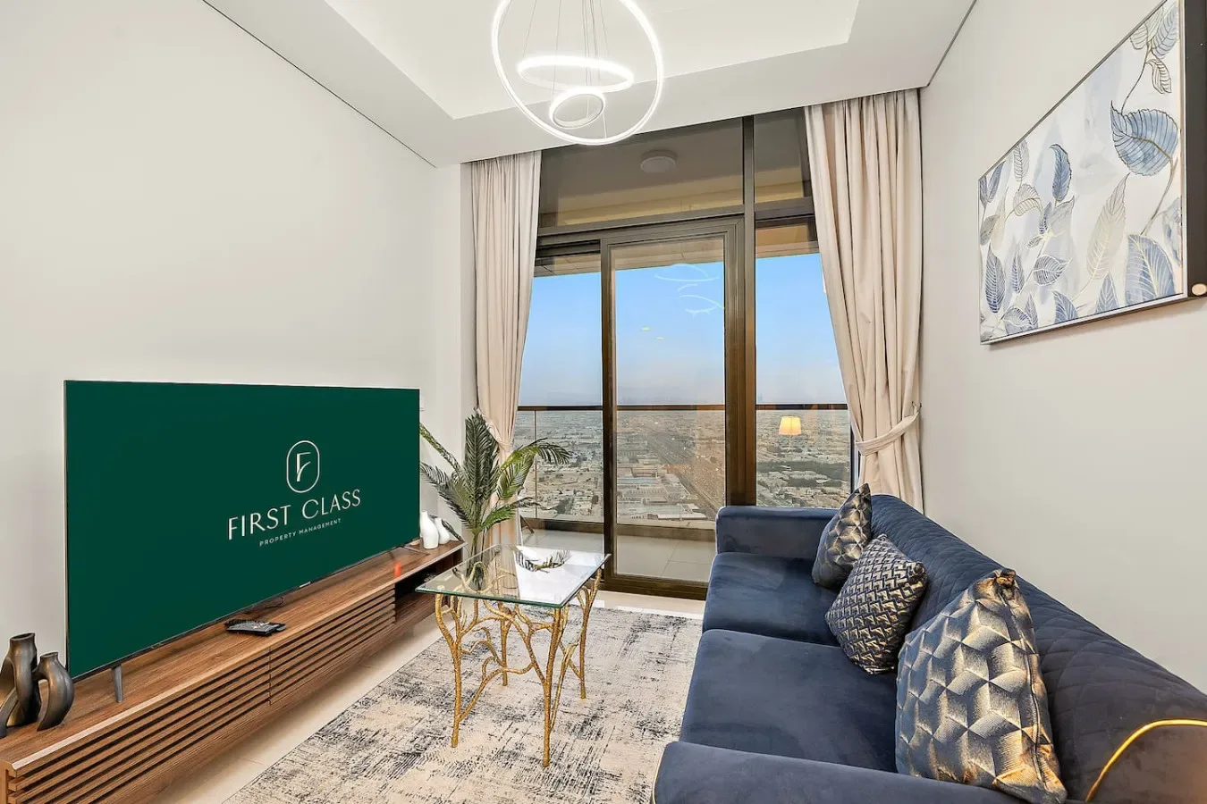 Una sala de estar con sofá azul, televisor y grandes ventanales con vistas a la ciudad.