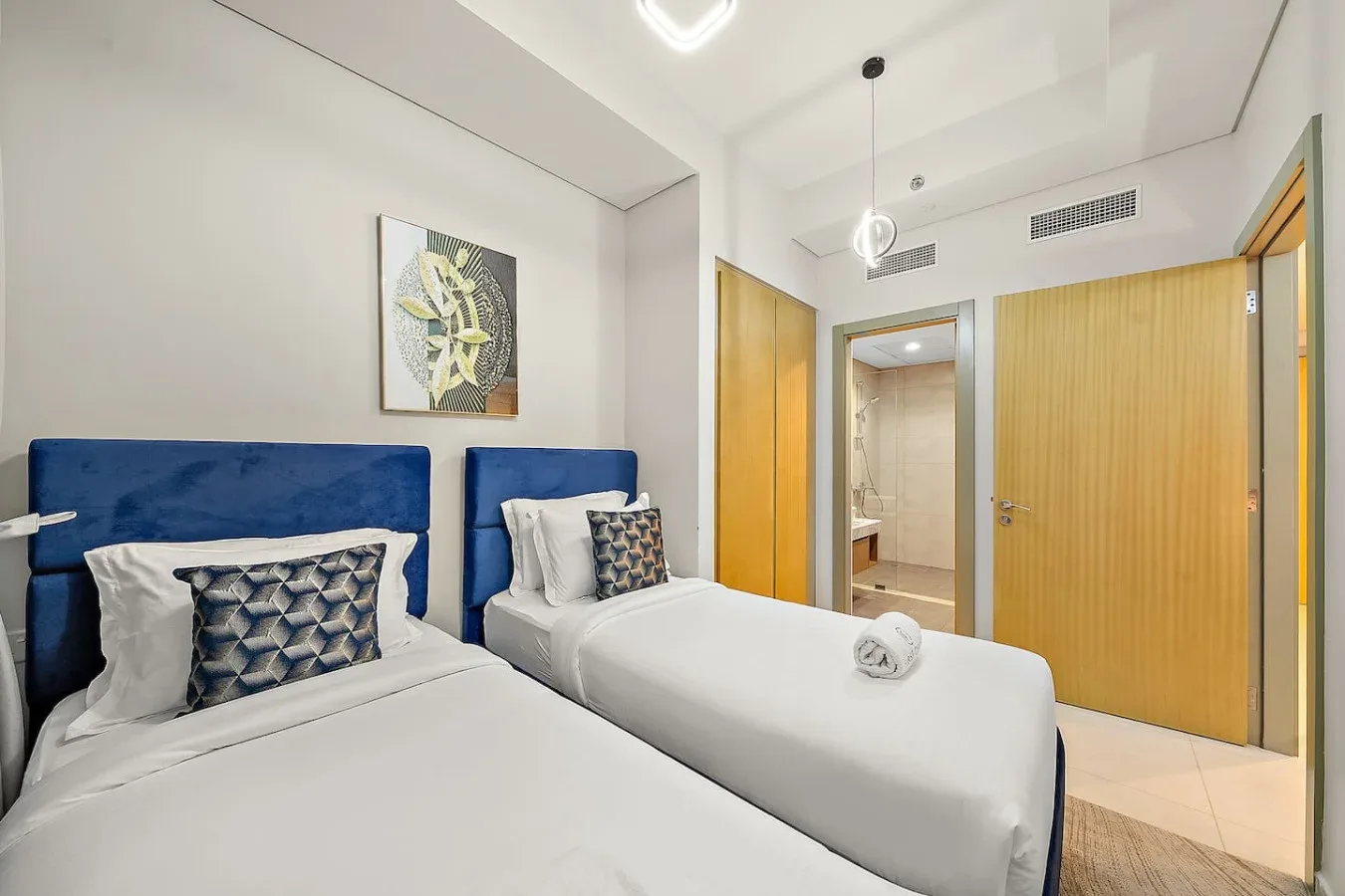 Un dormitorio con dos camas, cabeceros azules y una puerta al baño.
