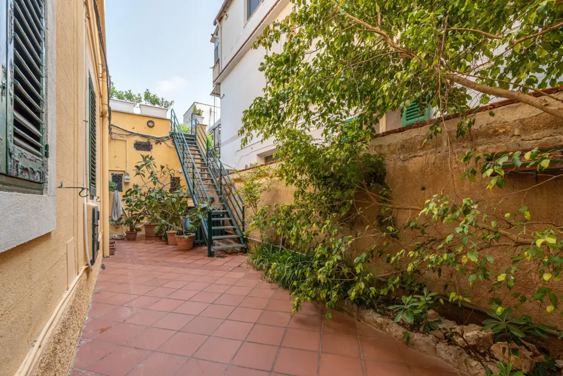 A tiled courtyard with a metal staircase and leafy plants along the walls.