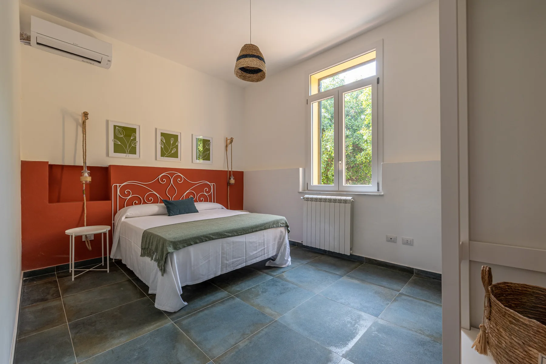 A bedroom with a bed, red accent wall, and a window.