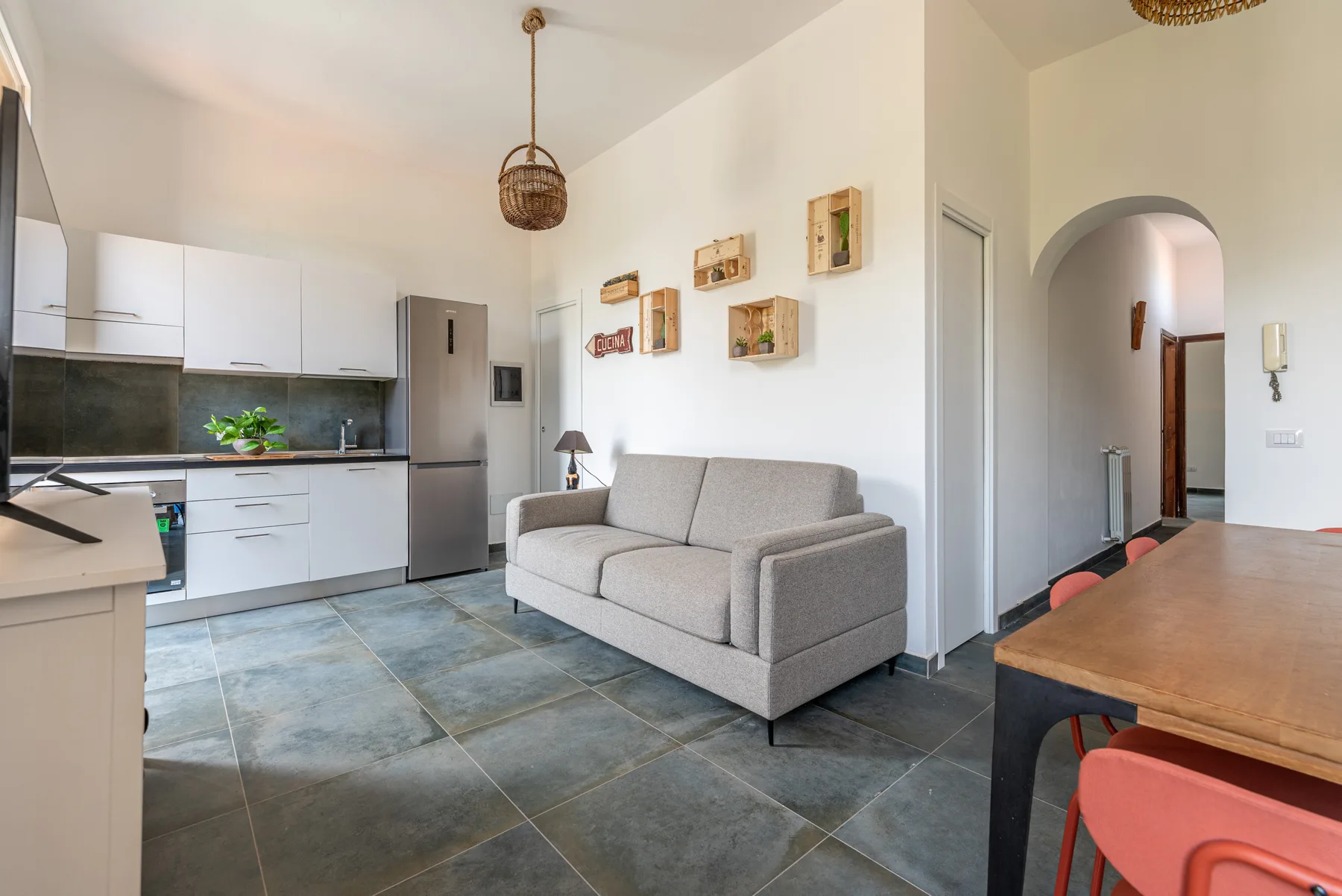 Una luminosa sala de estar y comedor con sofá gris, gabinetes blancos y una mesa de madera.