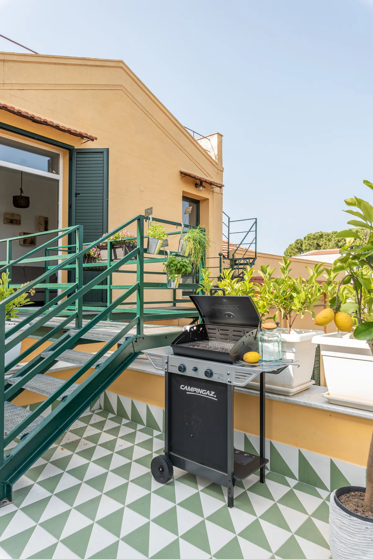 Una terraza soleada con una parrilla y suelo de baldosas geométricas verdes.