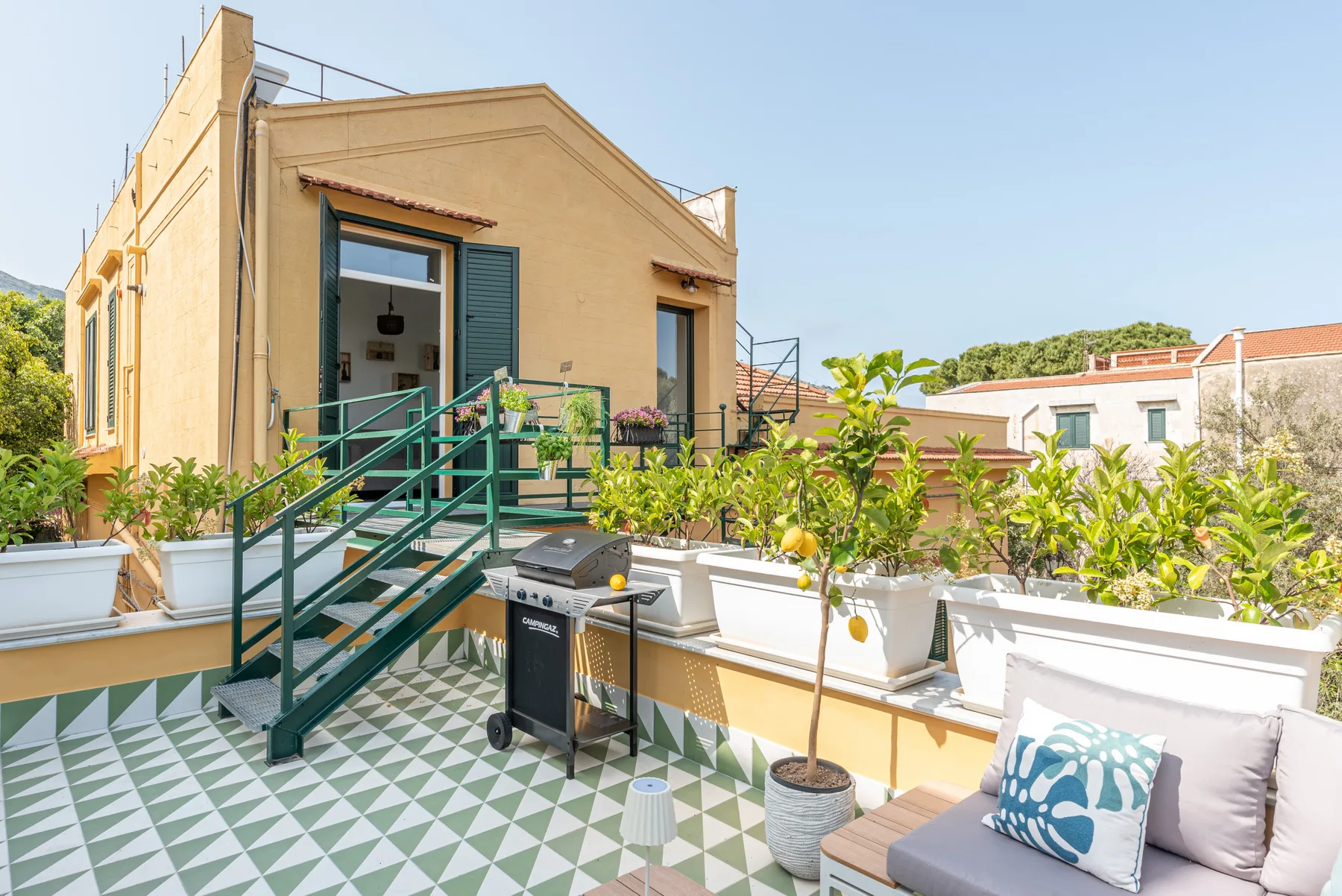 Una terraza soleada con baldosas estampadas, plantas en macetas y asientos al aire libre.