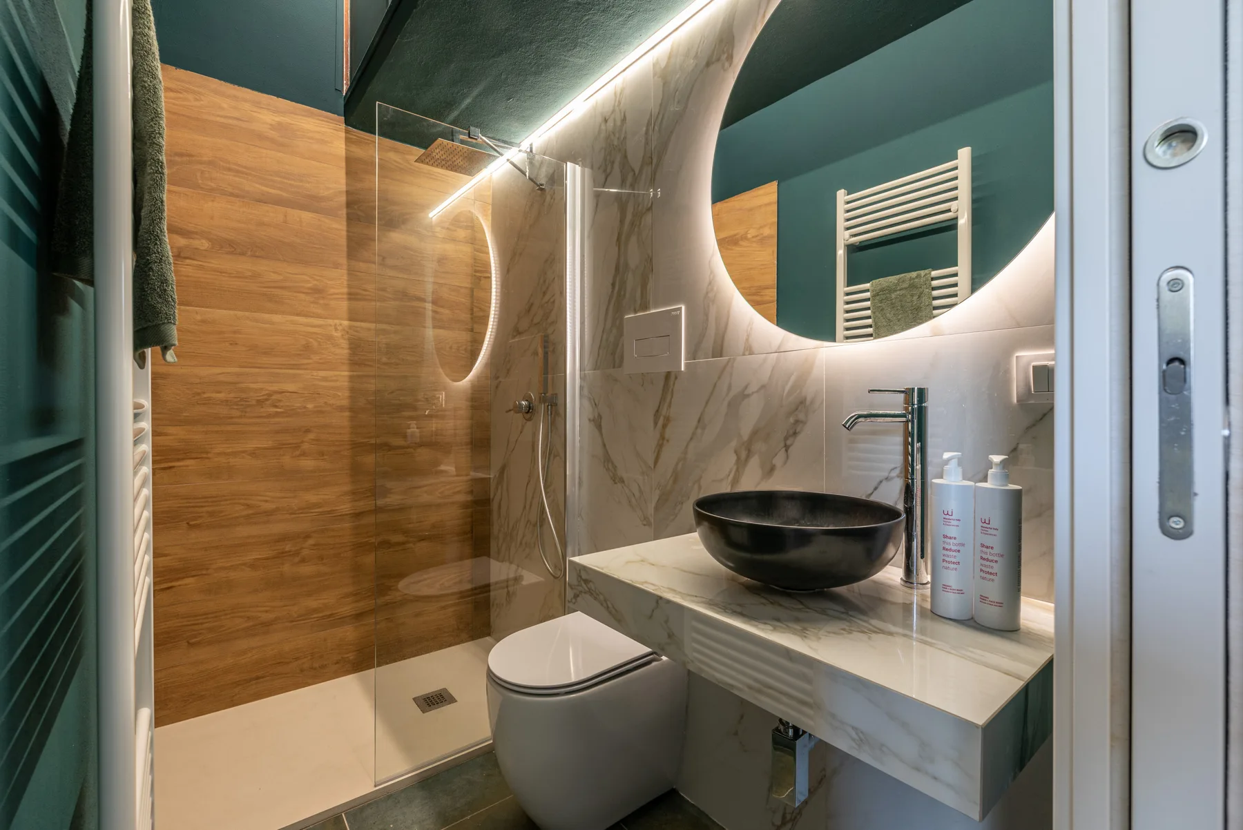 A bathroom with a glass shower, toilet, and a sink beneath a large mirror.