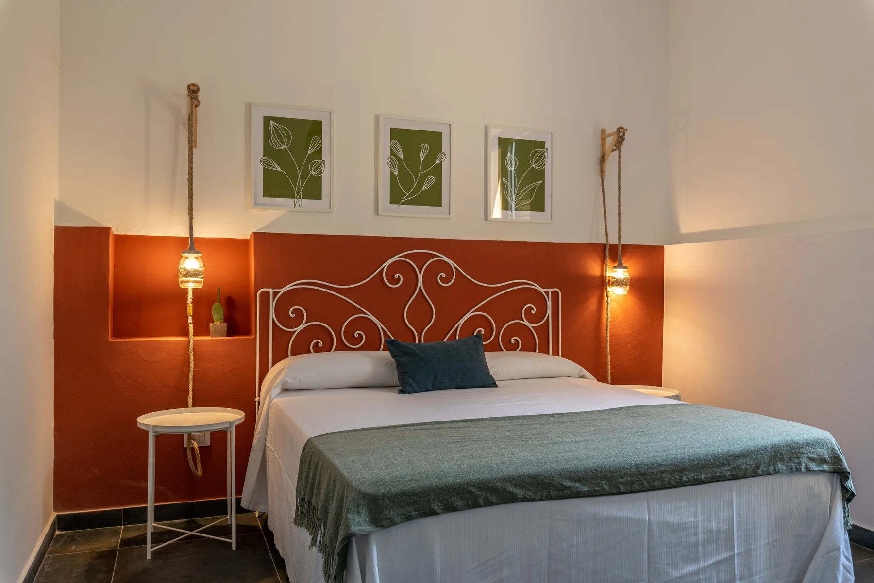 Un dormitorio con una cama doble, una colcha verde y láminas botánicas enmarcadas.