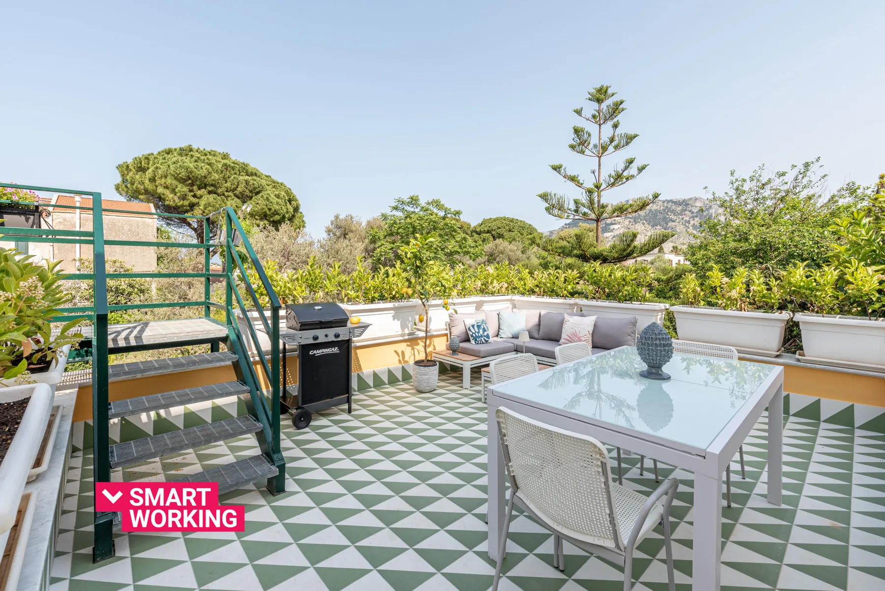 Una terraza al aire libre con mesa de cristal, asientos y suelo de baldosas estampadas.