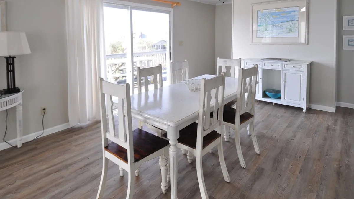 Un comedor luminoso tiene una mesa blanca con sillas junto a una puerta corrediza de vidrio.