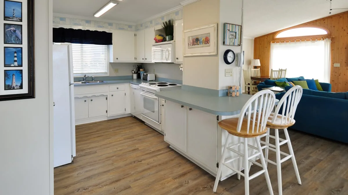 A bright kitchen with white cabinetry and a counter opening to a dining area.