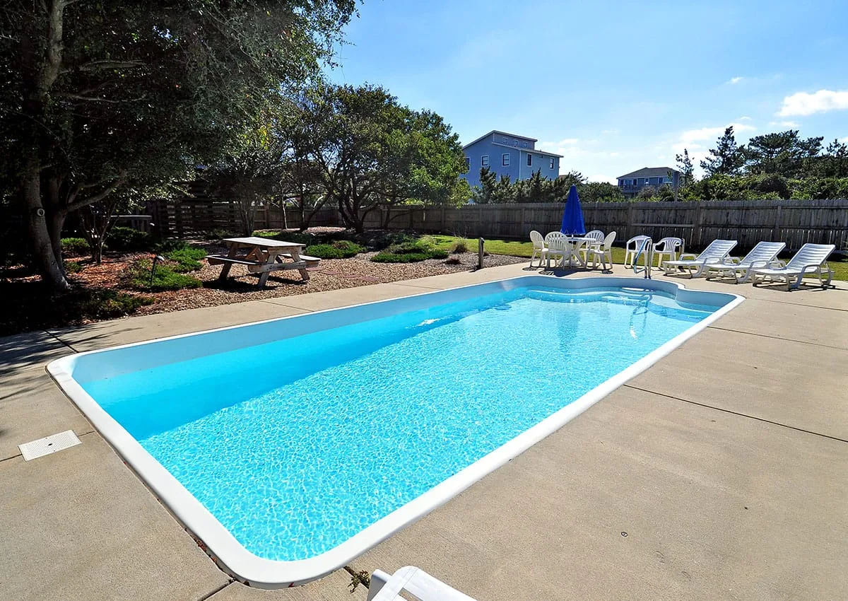 An outdoor swimming pool is surrounded by a sunny paved deck and lounge seating.